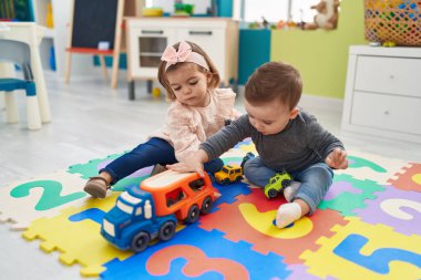 Sevimli çocuk ve kız arabalarla oynuyorlar. Anaokulunda yerde oturuyorlar.