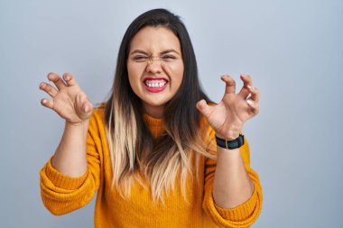 Soyutlanmış arka planda duran genç İspanyol kadın komik bir şekilde kedi gibi pençe hareketi yapıyor, saldırgan ve seksi bir ifade. 