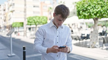 Young caucasian man using smartphone with serious expression at coffee shop terrace
