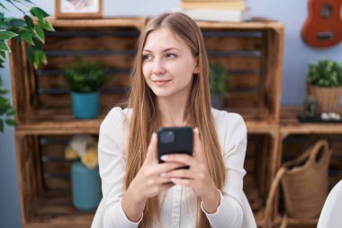 Beyaz kadın akıllı telefon kullanıyor. Evdeki masada oturuyor.