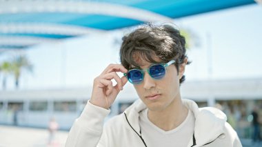 Parkta güneş gözlüğü takan, ciddi bir suratı olan genç bir İspanyol.