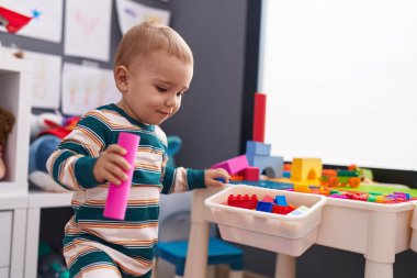 Sevimli beyaz bebek anaokulunda duran inşaat bloklarıyla oynuyor.