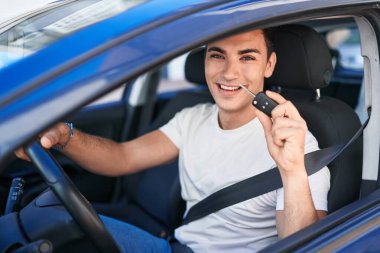 Young hispanic man smiling confident holding key of new car at street