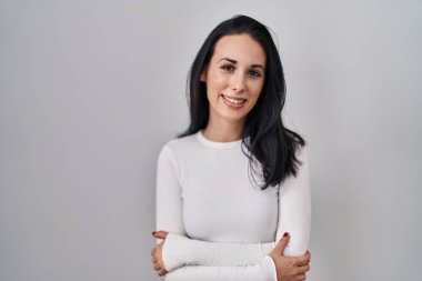 Hispanic woman standing over isolated background happy face smiling with crossed arms looking at the camera. positive person. 