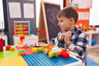 Anaokulundaki masada oturan beyaz çocuk inşaat bloklarıyla oynuyor.