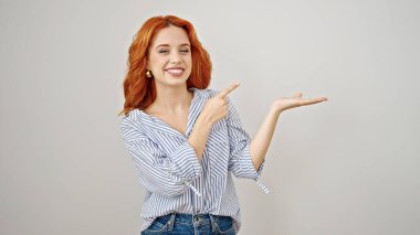 Genç, kızıl saçlı, gülümseyen bir kadın, yalıtılmış beyaz bir arka plan sunuyor.