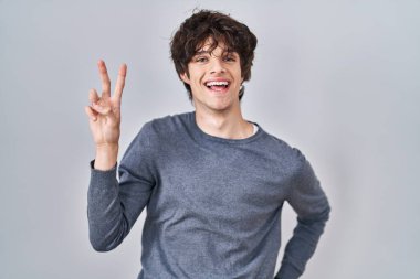 İzole edilmiş arka planda duran genç adam kameraya bakıp zafer işareti yapıyor. İki numara.. 