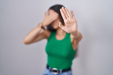 İzole edilmiş arka planda duran genç bir kadın elleriyle gözlerini kapatıyor ve üzgün ve korku ifadeleriyle jest yapıyor. utangaç ve olumsuz kavram. 