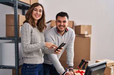 Man and woman ecommerce business workers writing on book using smartphone at office