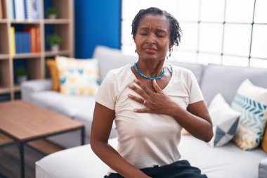 Middle age african american woman sitting on sofa suffering heart attack at home