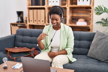 Afrikalı Amerikalı bir kadın danışma ofisinde online seans yapıyor. Kendini mutlu ve gururlu bir şekilde gösteren birini işaret ediyor. 