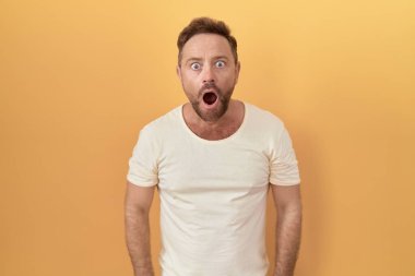 Sarı arka planda duran orta yaşlı bir adam şaşkınlık ve şaşkınlık dolu bir ifade, korku ve heyecan dolu bir yüz.. 