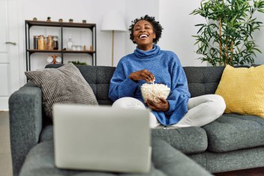 Afro-Amerikalı kadın evde kanepede oturmuş film izliyor.