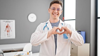 Genç İspanyol doktor gülümsüyor klinikte elleriyle kalp hareketi yapıyor.