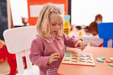 Anaokulunda matematik bilmecesiyle oynayan sevimli sarışın kız.