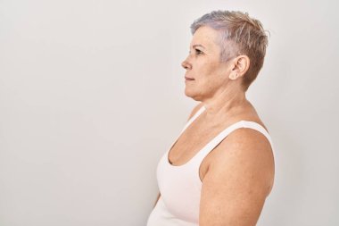 Beyaz arka planda duran orta yaşlı beyaz bir kadın. Yan tarafa bakıyor, rahat bir poz veriyor. Kendine güvenen bir gülümsemesi var.. 