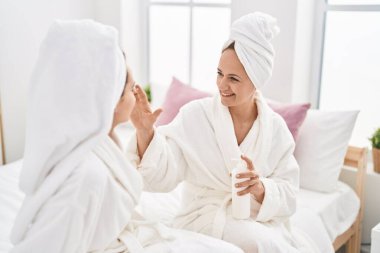Two women mother and daughter wearing bathrobe applying skin treatment at bedroom