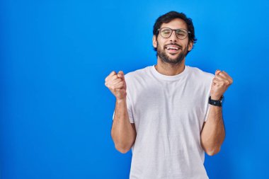 Mavi arka planda duran yakışıklı Latin adam kollarını kaldırmış ve gözleri kapalı zaferi kutluyor. Kazanan konsept. 