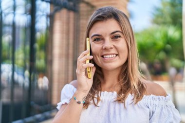 Gülümseyen genç bir kadın caddedeki akıllı telefondan konuşuyor.
