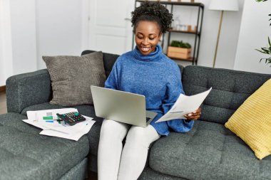 African american woman reading document using laptop accounting at home
