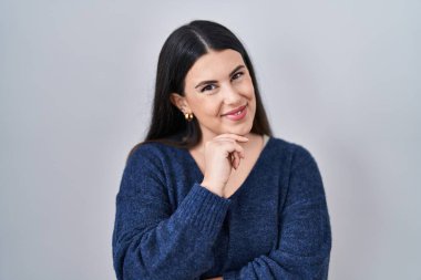 Genç esmer kadın izole edilmiş arka planda duruyor kameraya bakıyor kollarını kavuşturup ve çenesini kaldırarak gülümsüyor. Olumlu düşünmek. 