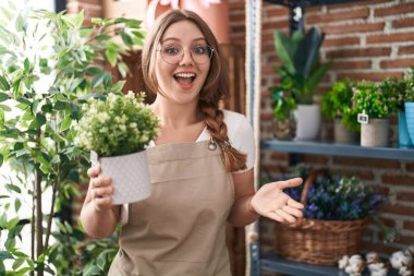 Çiçekçi dükkanında çalışan beyaz bir kadın mutluluğu kutluyor. Gülümsüyor ve el kaldırıyor. 