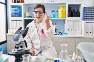 Hispanic girl with down syndrome working at scientist laboratory showing middle finger, impolite and rude fuck off expression 