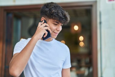 Latin kökenli genç, gülümsüyor ve caddede akıllı telefondan konuşuyor.