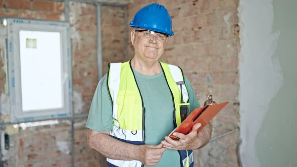 中年人白发苍苍的建筑工人微笑着在工地剪贴板上看到自信的阅读文件 — 图库照片