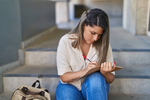 Young hispanic woman student writing on notebook at university