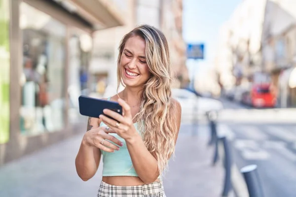 年轻的金发女人笑着自信地在街上看智能手机视频 — 图库照片