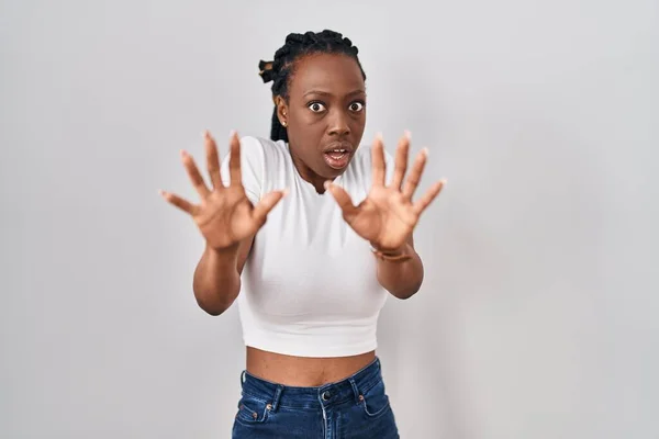 Beautiful black woman standing over isolated background afraid and terrified with fear expression stop gesture with hands, shouting in shock. panic concept.