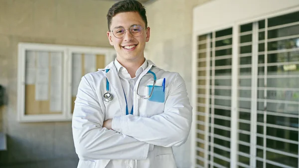 年轻的惊慌失措的医生微笑着 自信地站在医院里 双手交叉地做着手势 — 图库照片