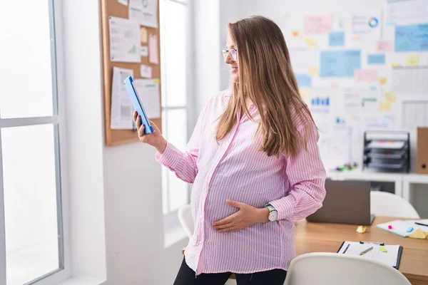 年轻的怀孕女工在办公室使用触摸板 自信地微笑着 — 图库照片