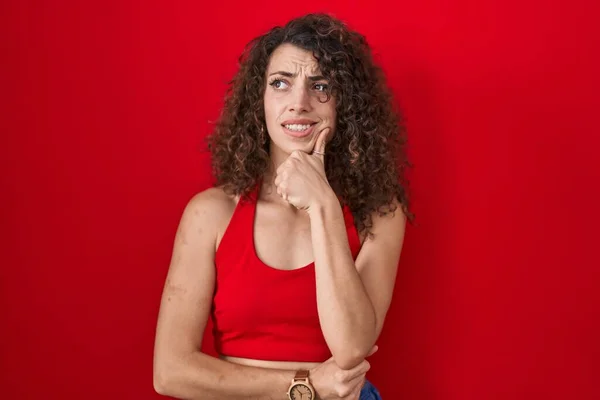 Kırmızı Arka Planda Duran Kıvırcık Saçlı Spanyol Kadın Bir Soru — Stok fotoğraf