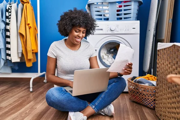 非洲裔美国妇女使用笔记本电脑阅读文书工作 在洗衣房等待洗衣机 — 图库照片