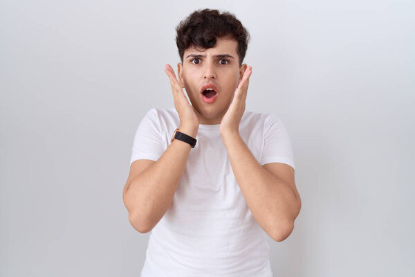 Young non binary man wearing casual white t shirt afraid and shocked, surprise and amazed expression with hands on face 
