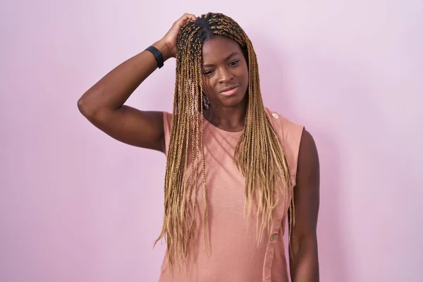 身穿辫子的非裔美国女人站在粉色的背景上 对问题感到困惑和疑惑 拿不定主意 手拿着头思考 沉思的概念 — 图库照片