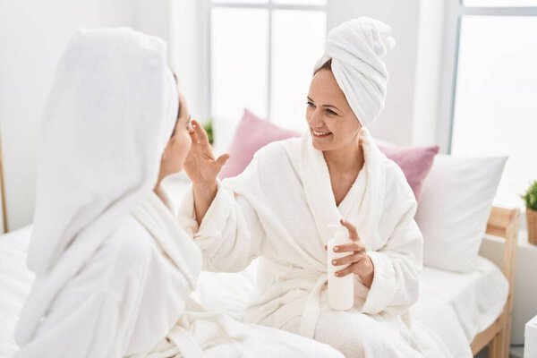 Two women mother and daughter wearing bathrobe applying skin treatment at bedroom