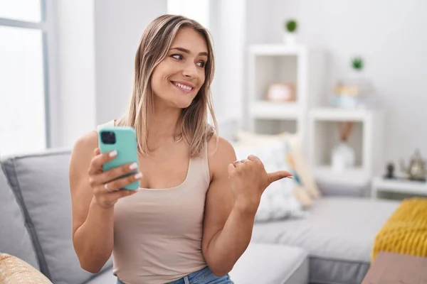 Blonde Caucasian 여성은 스마트폰 메시지를 사용하여 소파에 엄지를 옆으로 치켜들고 — 스톡 사진