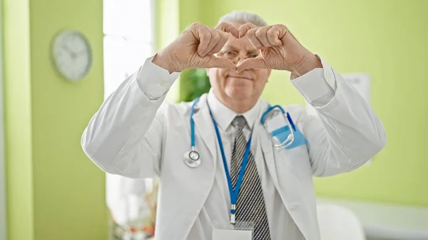 Μεσήλικας Γκριζομάλλης Γιατρός Χαμογελαστός Κάνοντας Χειρονομία Καρδιάς Χέρια Στην Κλινική — Φωτογραφία Αρχείου