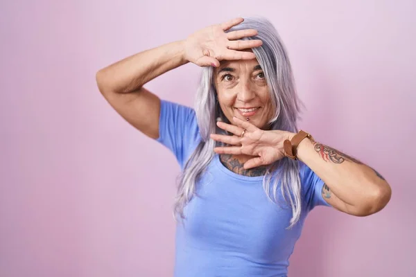 stock image Middle age woman with tattoos standing over pink background smiling cheerful playing peek a boo with hands showing face. surprised and exited 