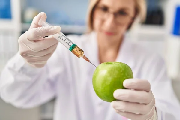年轻的金发女科学家在实验室把液体注入苹果中 — 图库照片