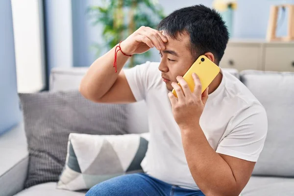 Joven Hombre Chino Hablando Teléfono Inteligente Con Expresión Preocupada Casa — Foto de Stock