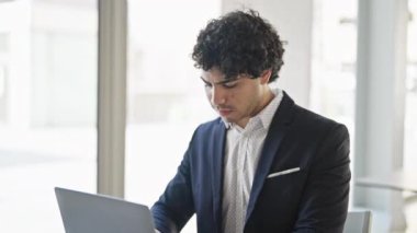Genç Latin iş adamı ofiste gülümseyen bir dizüstü bilgisayar kullanıyor.