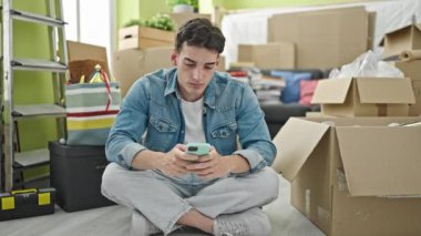 Genç İspanyol adam akıllı telefon kullanıyor. Yeni evine üzgün bakıyor.