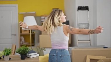 Sarışın, kendine güvenen genç bir kadın yeni evinde kollarını açmış kendi kendine dönüyor.