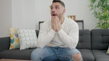 Young hispanic man stressed sitting on sofa at home