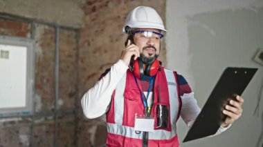 İnşaat alanında akıllı telefon okuyarak konuşan genç latin mimar.