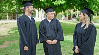 Bir grup insan, üniversite kampüsünde kendine güvenen bir şekilde sırıtarak mezun oldu.